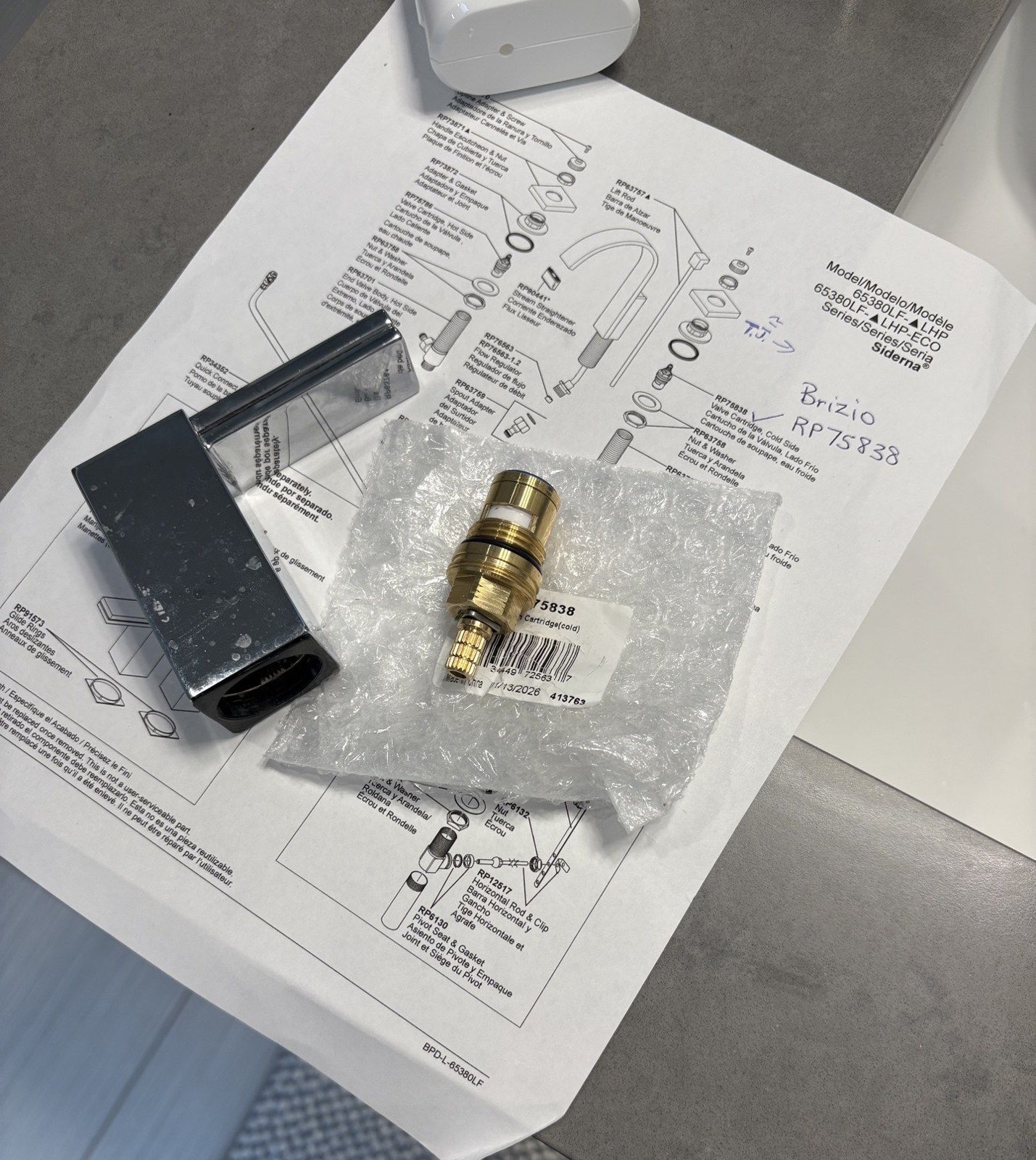 A new brass ceramic faucet cartridge in a plastic bag on a printed faucet parts diagram, next to a removed chrome lever handle