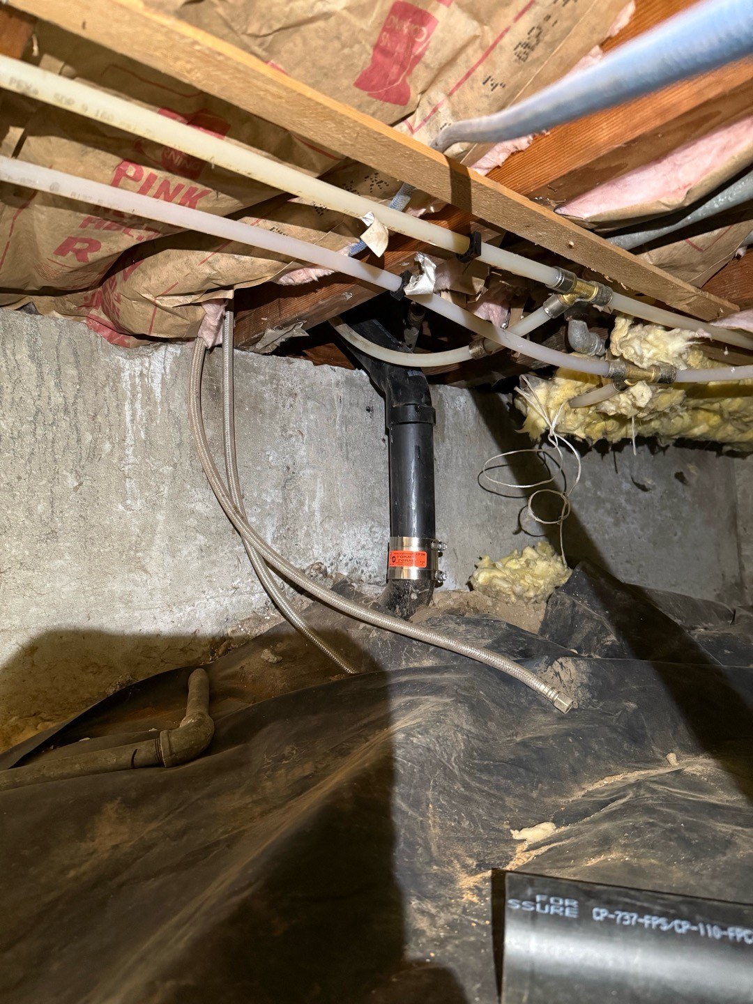New black ABS branch drain and stainless no-hub coupling installed in a Shoreline crawlspace beneath insulated floor joists