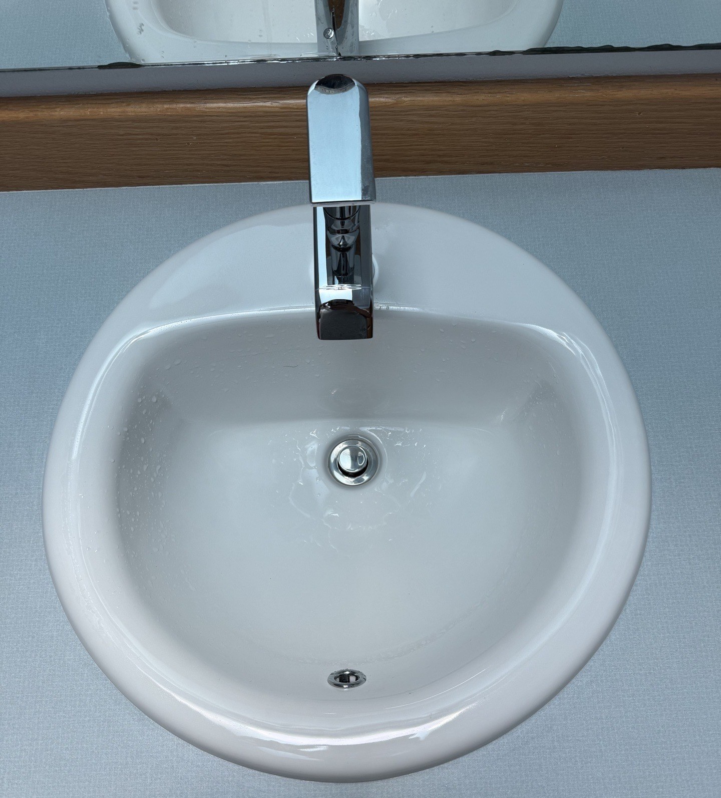 A round white bathroom sink set into a grey laminate counter with a modern chrome single-lever faucet and a new pop-up drain