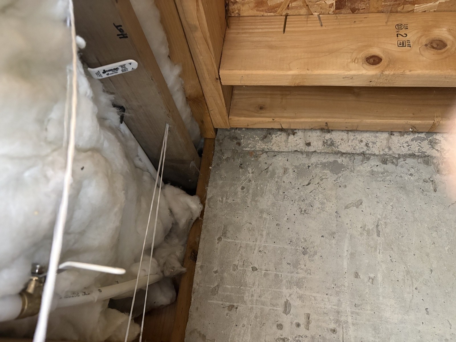 Opened wall cavity behind the spigot showing the white PEX supply line and its brass shutoff valve among insulation